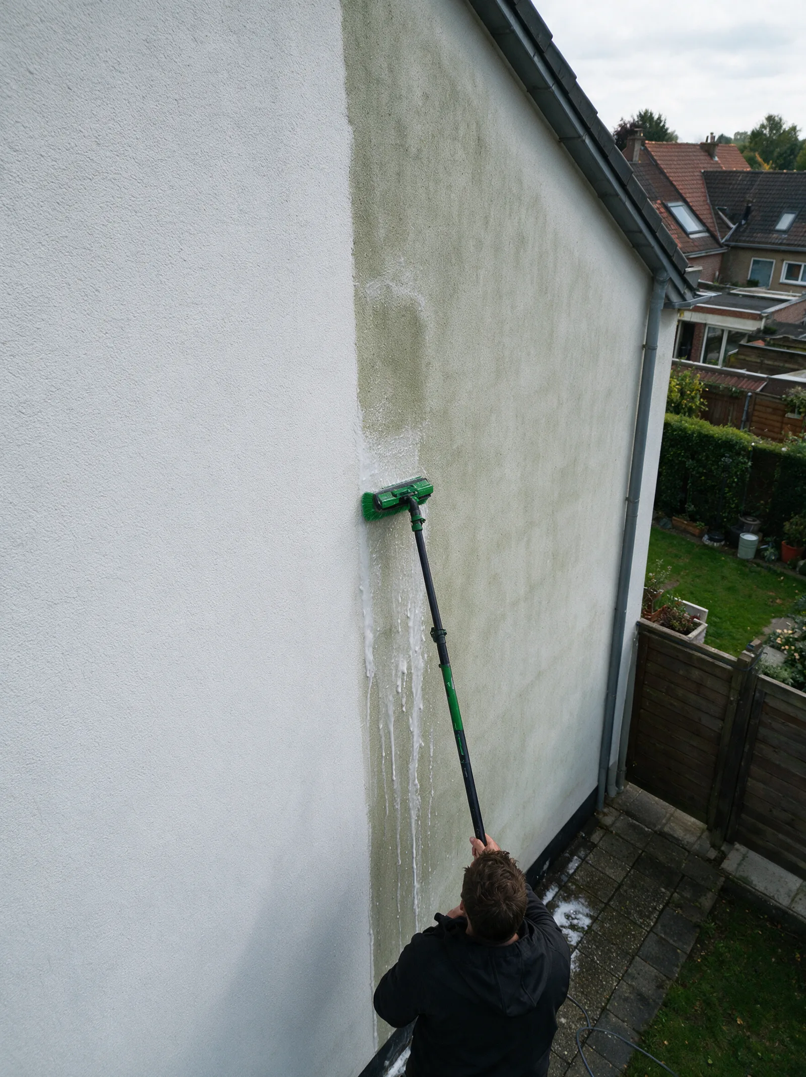 Zijgevel in crepi, halverwege de reiniging: links nog groen, rechts weer wit